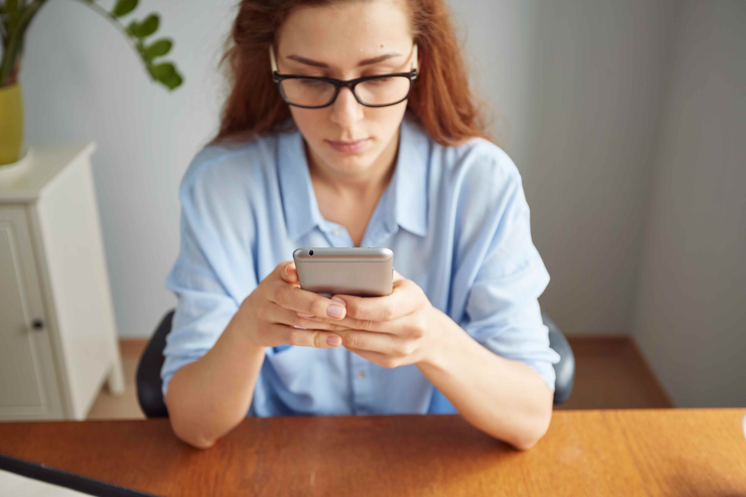 cropped-view-portrait-cute-redhead-girl-texting-cell-phone-wooden-desk-11zon